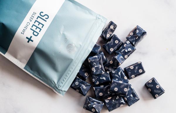 Lifestyle shot of Sleep+ Wellness Chews spilling out of the bag on to a white table.